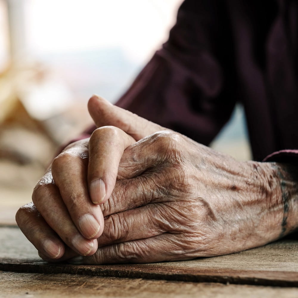 Old hands resting on a wooden table with folded hands.