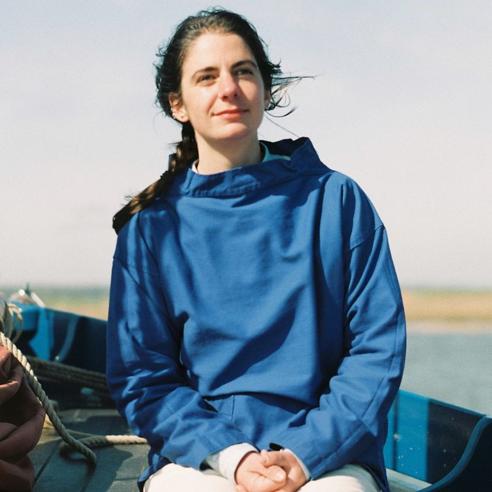 Rose Ravetz, sitting on a boat wearing a sailing smock and with the wind blowing in her hair