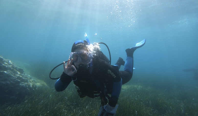 Russell Smart diving in a deep blue sea, he is holding up the ok symbol in his hands