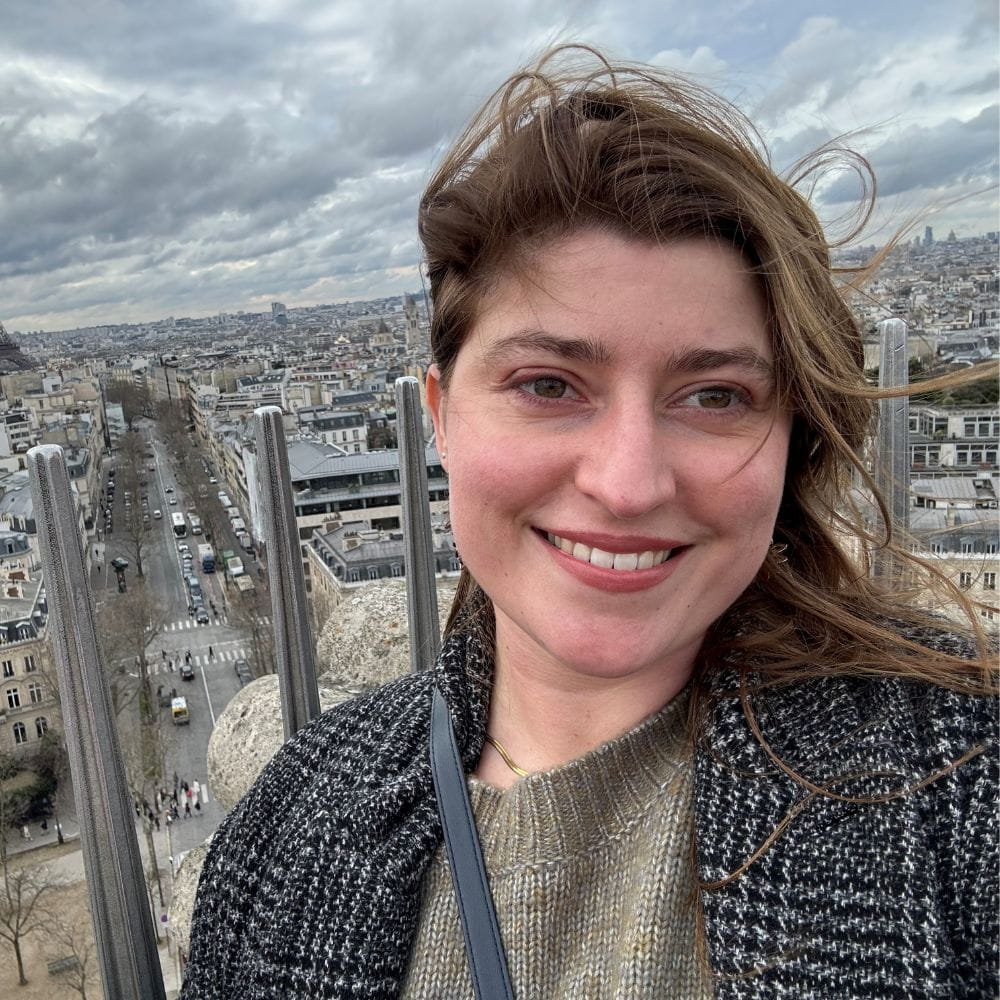 Sarai Lambert standing on a tall building in Paris which overlooks the Eiffel Tower
