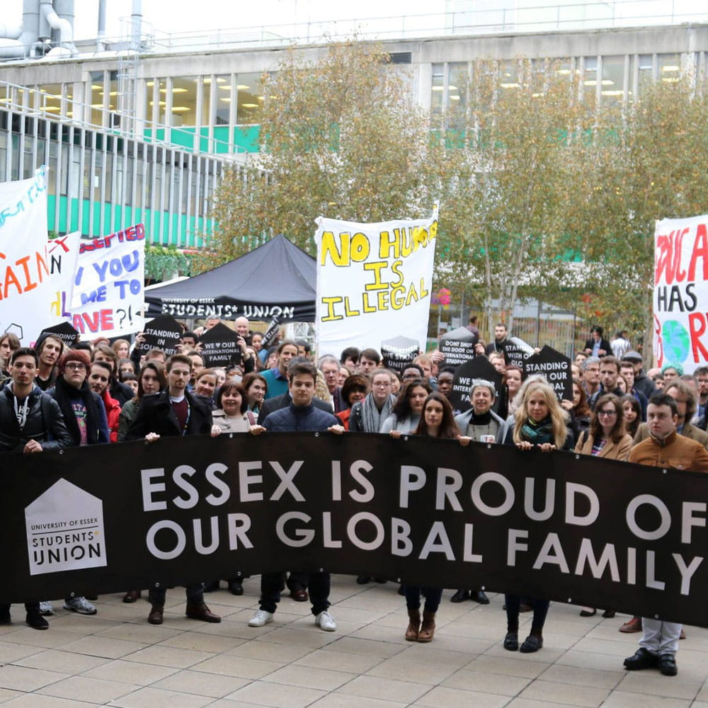 Student gathering on campus with large banner 'essex is proud of our global family'