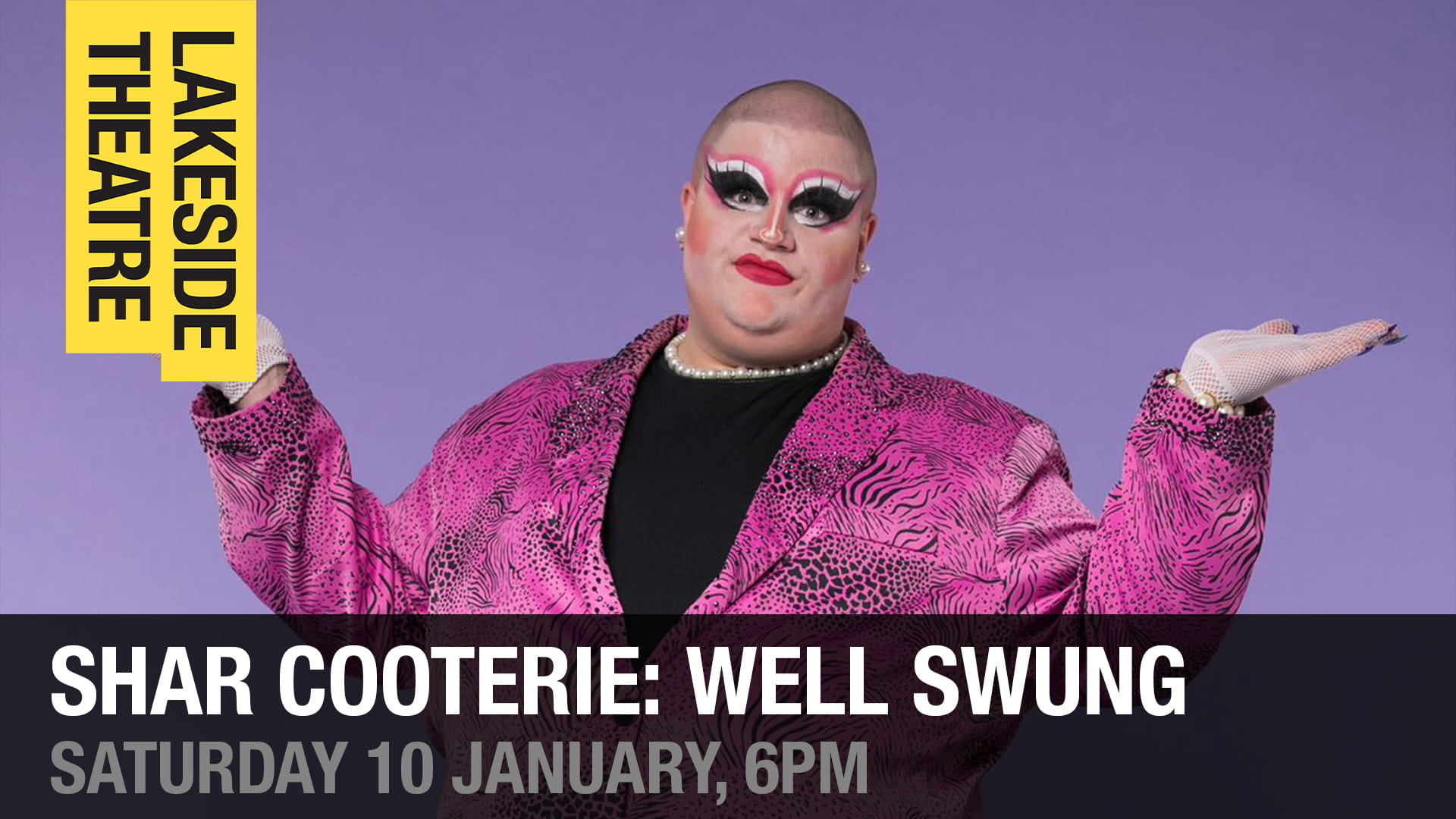 Drag Queen Shar Cooterie stands wearing full drag make up but with no wig and a fabulous pink tiger-print jacket in front of a purple backdrop.