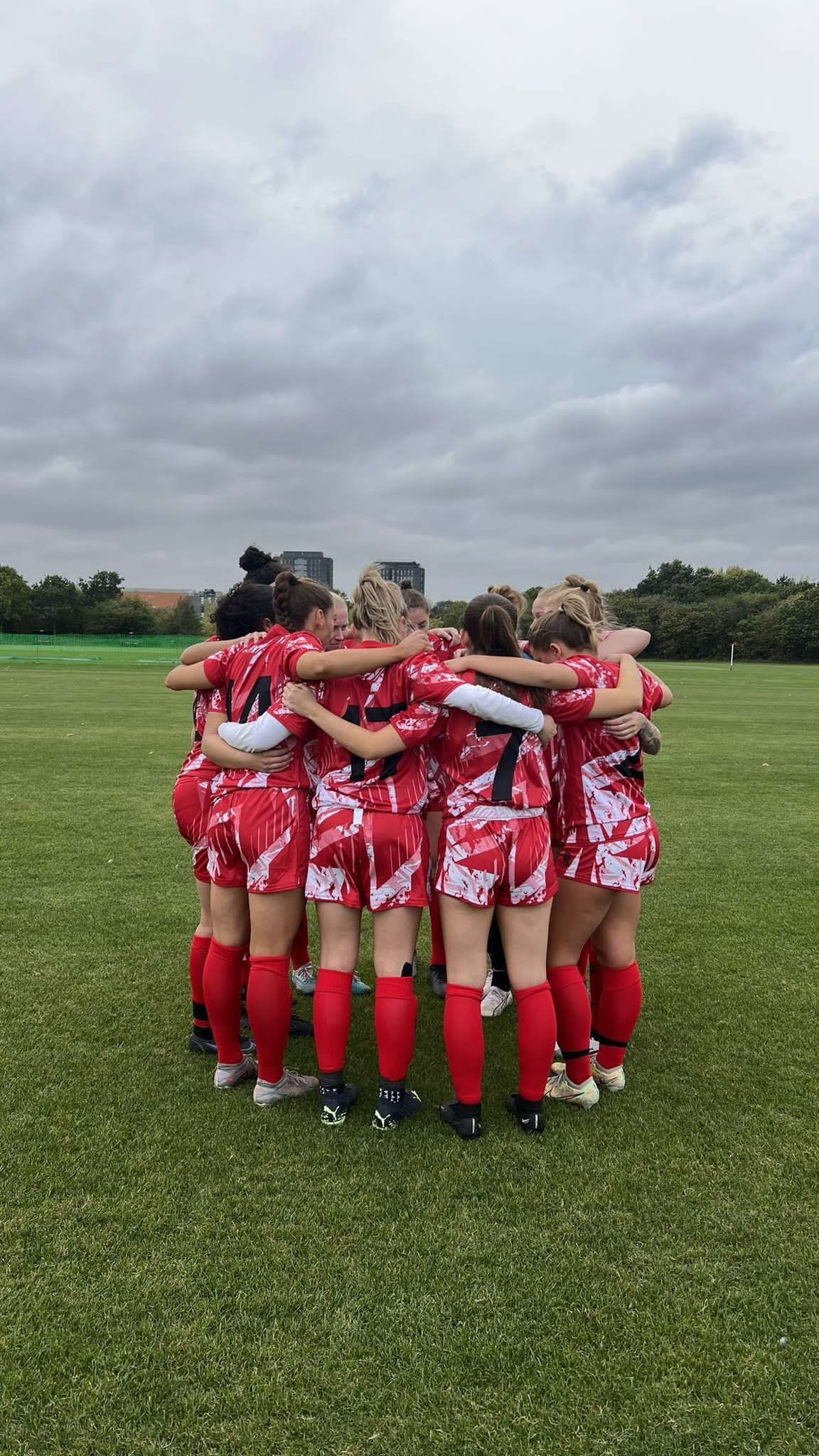 members of the womens football team, group hugging on pitch