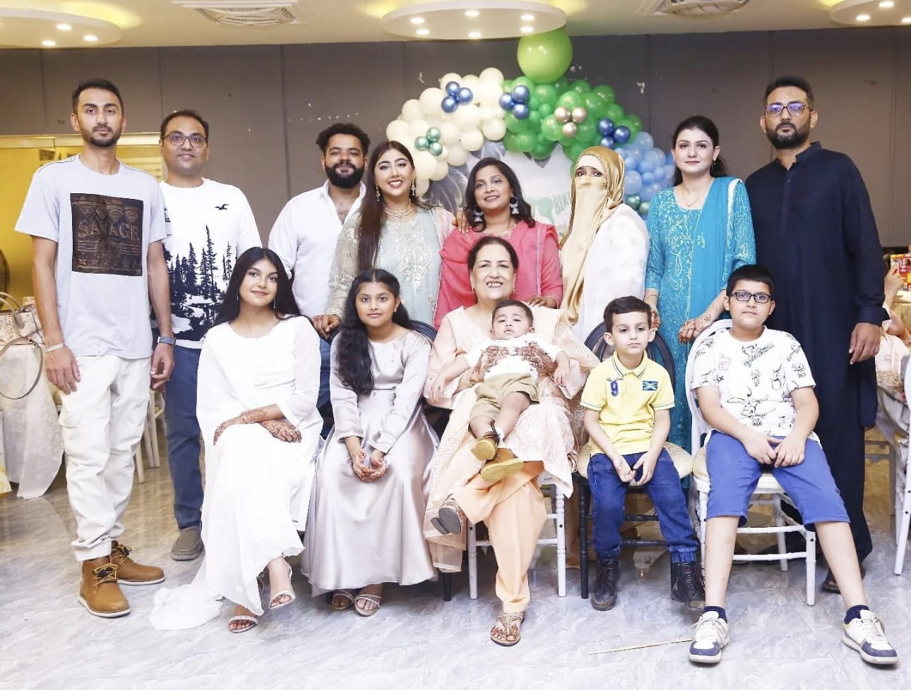 Marium Masroor lines up for a family photo with white, green, blue, and gold balloons behind the group.