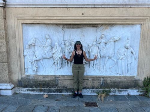 Nadia de Oliveira Coutinho standing in front of a wall frieze in Bologna