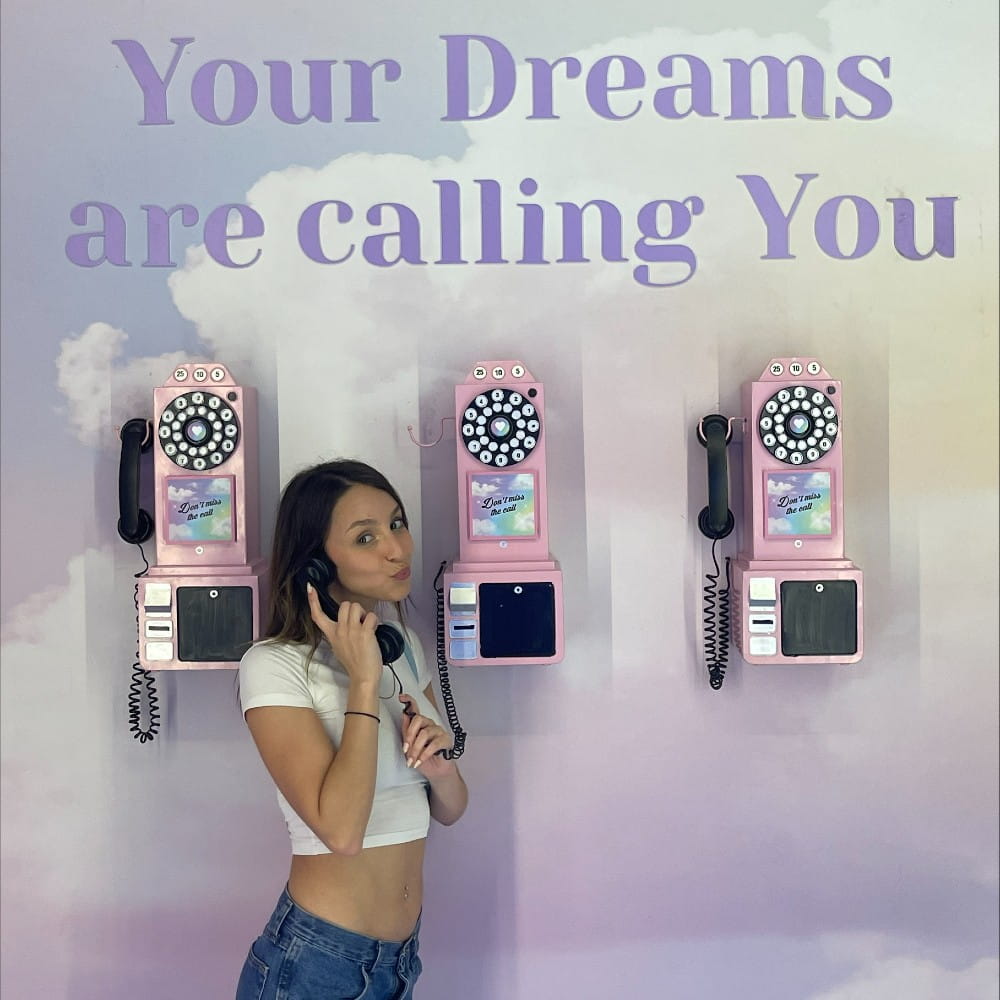A female stood in front of three phones with the text "your dreams are calling you" written above