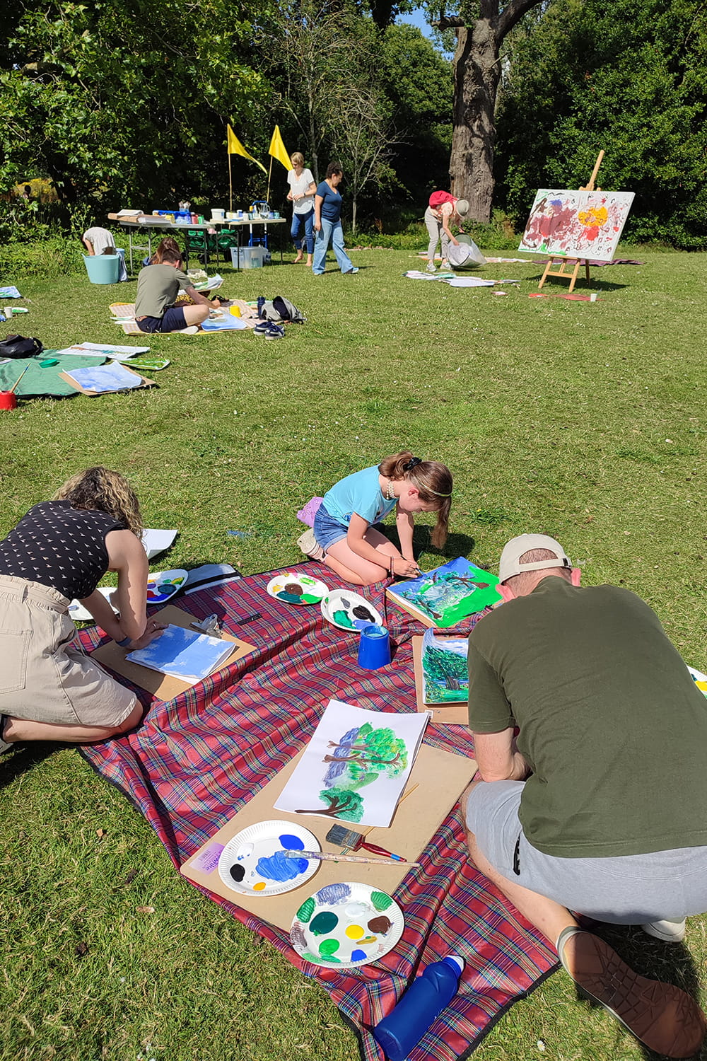 groups of families sit on blankets in wivenhoe park painting togehter