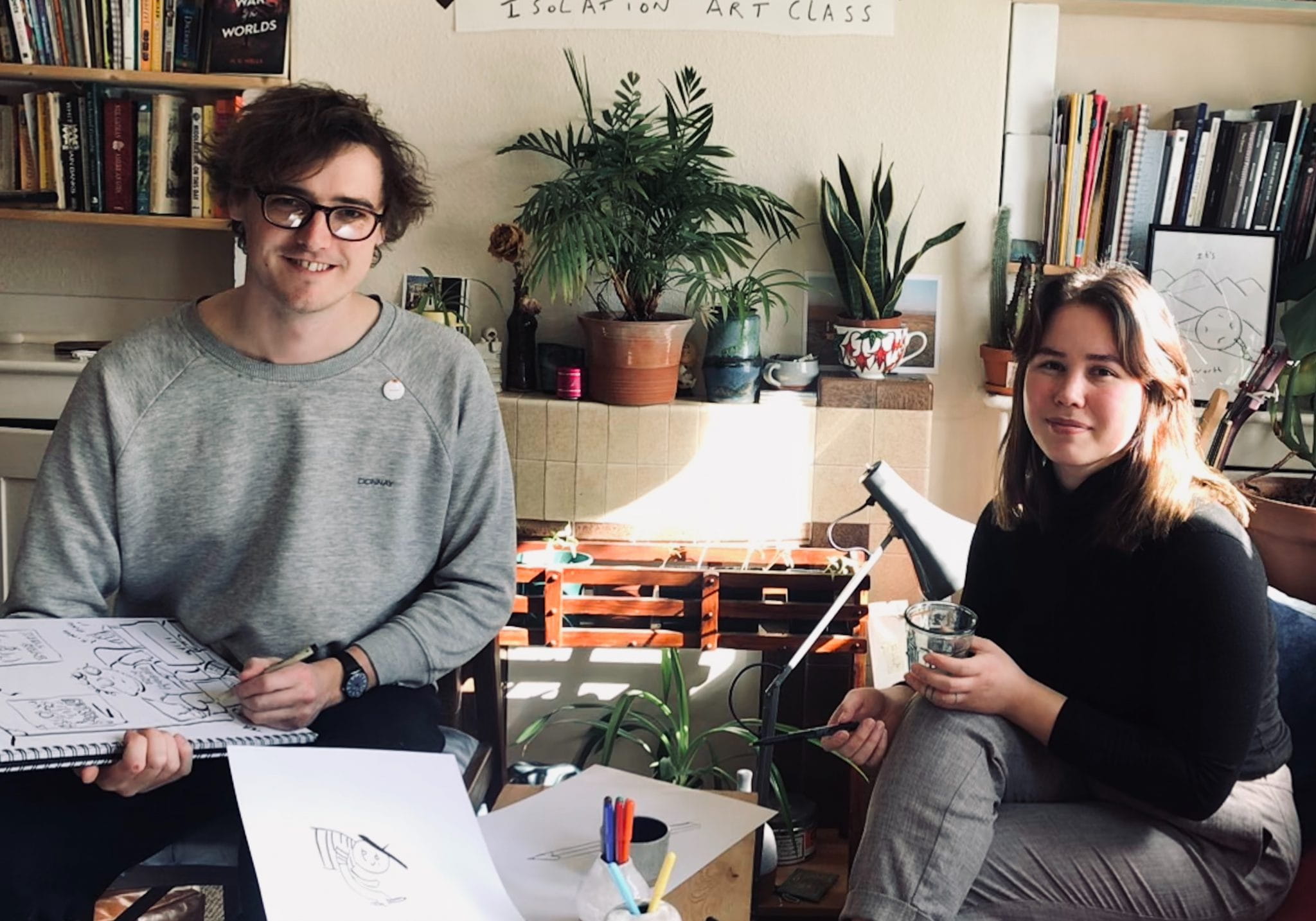 Artists Tom and Iris sit in their living room surrounded by their artists tools