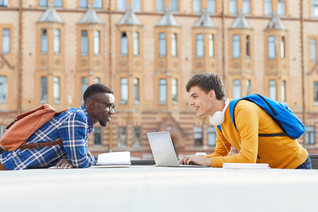 Two students with laptops looking at eachpther