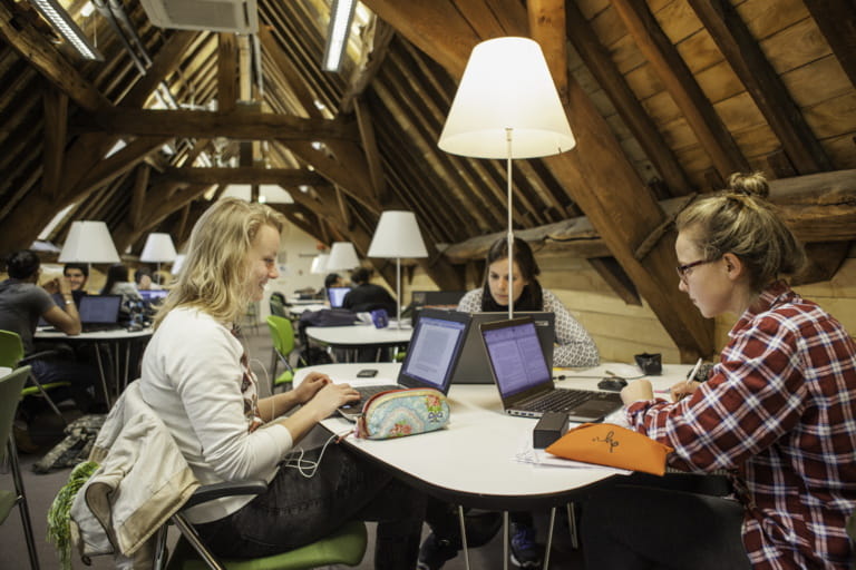 3 female students sitting round table looking at their laptops