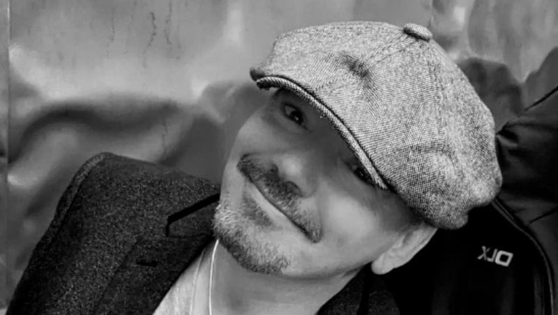 John-Francis Nero photographed at an angle, smiling and wearing a flat cap.