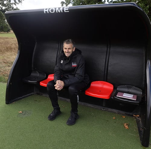 University of Essex Performance Football Coach Pawel Guziejko sitting in the grounds' Home dugout 