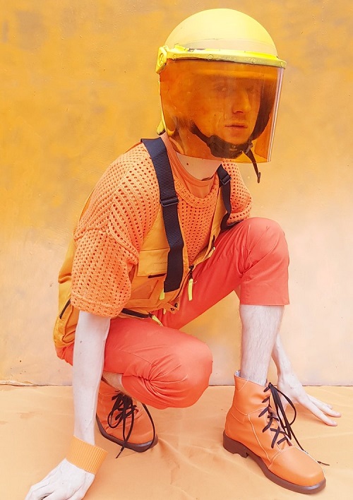 George Morl dressed in orange clothing and boots, with a yellow helmet and orange visor, crouched down.