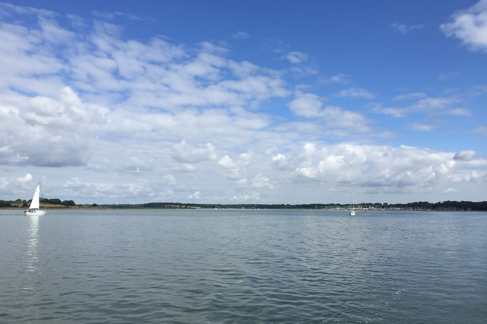 The Blackwater estuary, with puffy clouds in blue skies and a boat with a sail visible in the distance on the left.