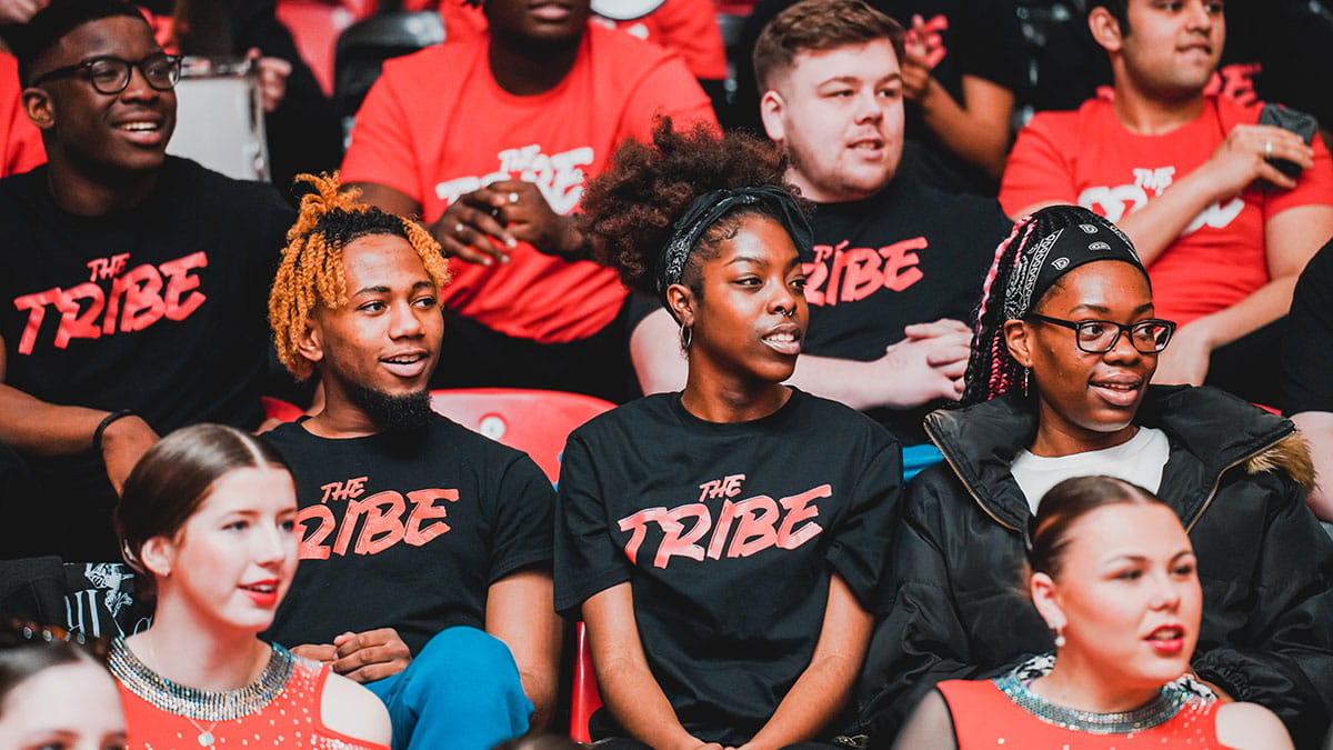 Students watching a Rebels game wearing black and red Tribe tshirts)