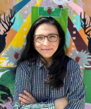 Dr Lisette Farias Vera standing with her arms folded in front of a colourful background.