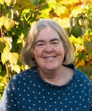 Professor Wendy Bryant in front of autumn-coloured foliage.