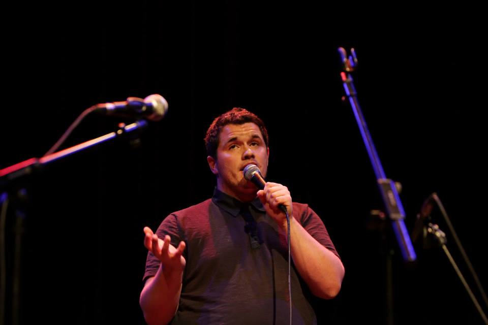 A performer speaking into a microphone, on stage. 