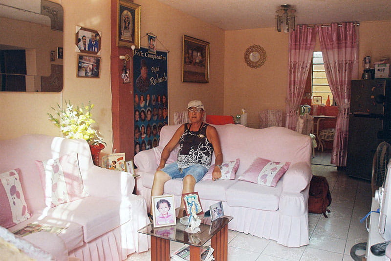 Lead image of the exhibition Taking a Bow by artist Bryan Giuseppi Rodriguez. Bryan's grandfather is sat on a pink sofa, in his pink living room. 